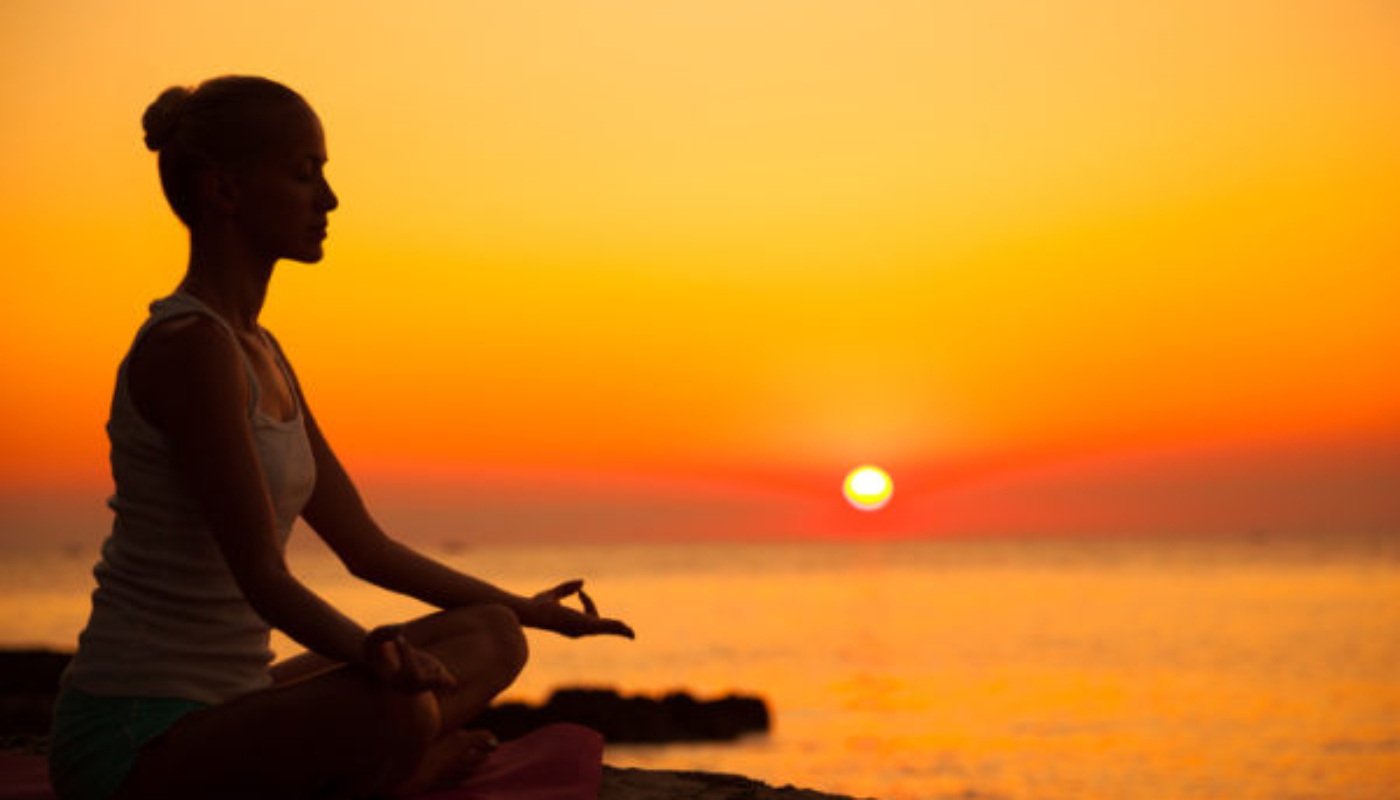 Young woman meditating at sunset . Sitting in lotus position outdoors . Dusk.