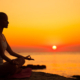 Young woman meditating at sunset . Sitting in lotus position outdoors . Dusk.